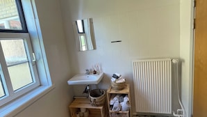 Un baño pequeño y limpio, con ventana, lavamanos, espejo, radiador y cestas de almacenamiento.