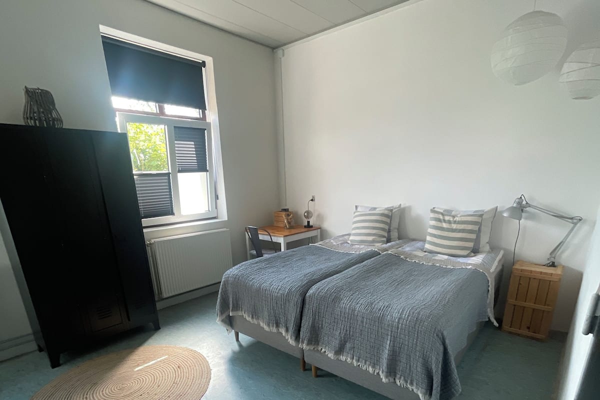 A bedroom with a bed, two bedside tables, a desk, a lamp, and two woven mats on the floor.