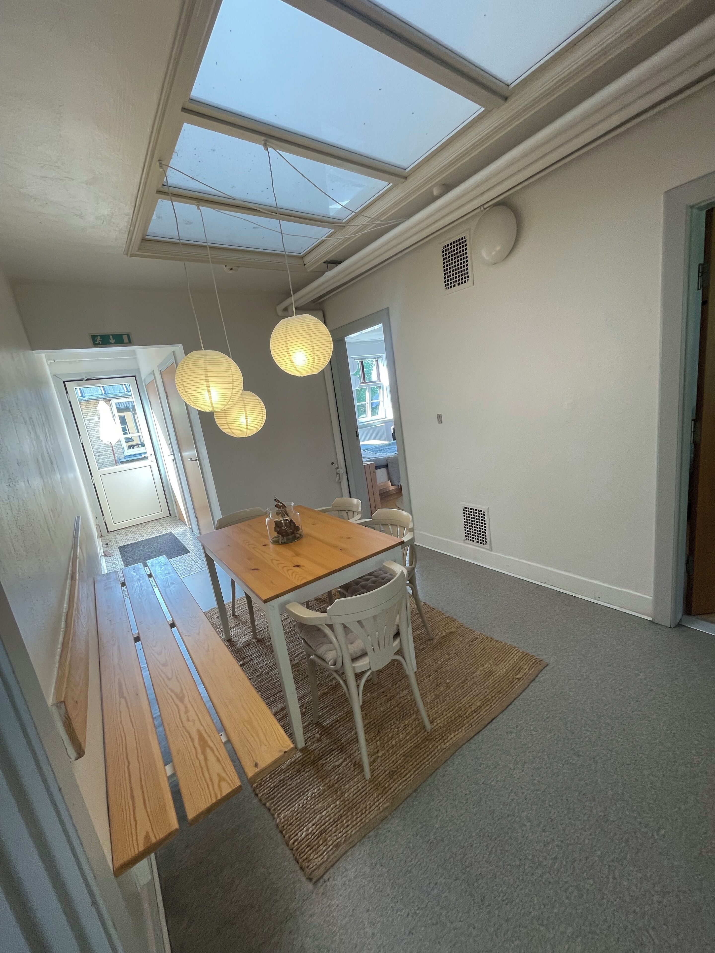 Uma sala de jantar com mesa de madeira e cadeiras brancas, um claraboia acima e vista para o exterior.