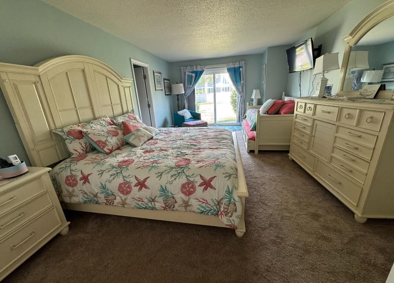 Een slaapkamer met een bloemenbedekker, een witte dressoir, een nachtkastje en een televisie aan de muur.