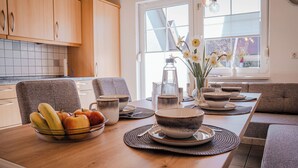 Et spiseområde med et træbord dækket til et måltid, inklusive skåle, tallerkener og en skål med frugt.