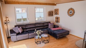 En moderne stue med en mørkegrå modulsofa, to runde sofaborde, en vase med blomster og trægulv.