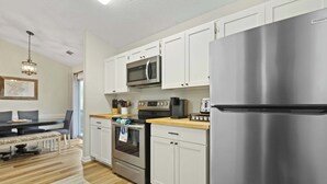 A modern kitchen with white cabinets, stainless steel appliances, and a wooden dining table. - Island Oaks - your perfect Savannah escape! (Savannah)