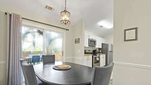 A dining area with a black table and four chairs, a chandelier, a kitchen with white cabinets, and a view through a large window. - Island Oaks - your perfect Savannah escape! (Savannah)