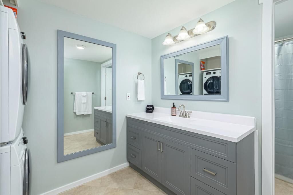 A bathroom with a large mirror, a vanity with a sink, and a shower area.