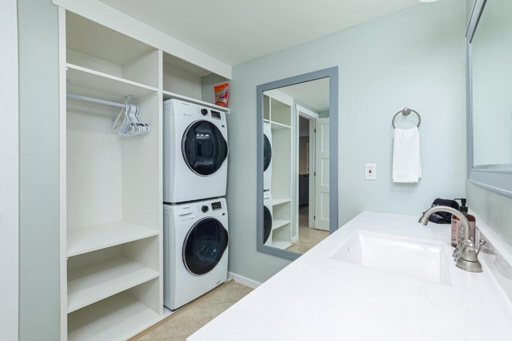 A laundry room with two stacked washing machines, a white sink, and a mirror above the sink.