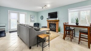 A living room with a sofa, a coffee table, a fireplace, and a dining area with chairs and a table. - The Alpine - Central Collingwood Condo (Collingwood)
