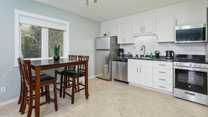 A modern kitchen with white cabinets, stainless steel appliances, and a dining area with a wooden table and chairs. - The Alpine - Central Collingwood Condo (Collingwood)