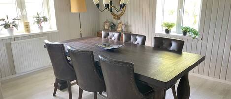 A dining area with a large table, six chairs, a chandelier, and potted plants.