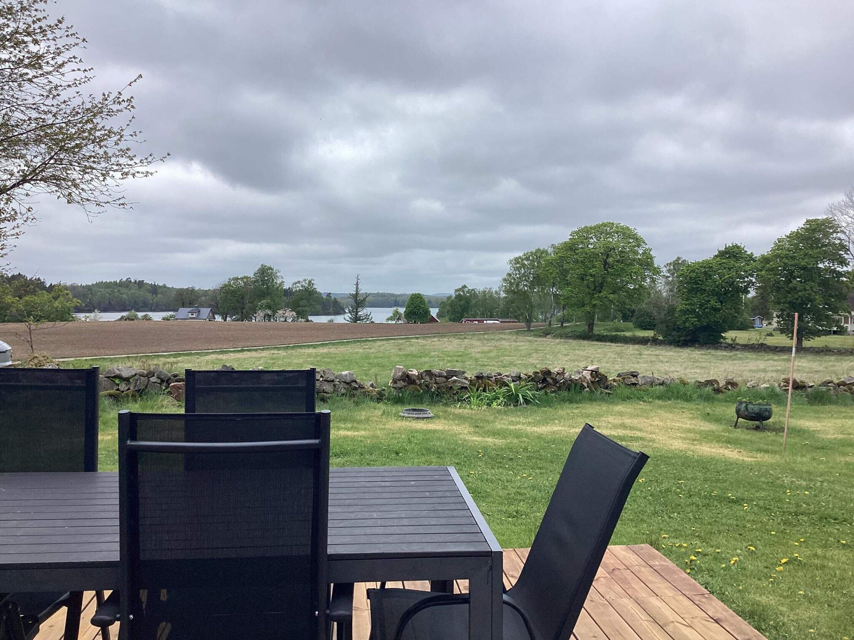 A deck with a table and chairs overlooking a grassy field with a lake and buildings in the distance.