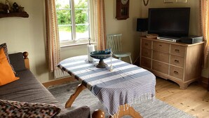 Ein gemütliches Zimmer mit einem Bett, einem Tisch mit gestreiftem Tischläufer, einem Fernseher, einer Uhr und einem Holzkabinett.