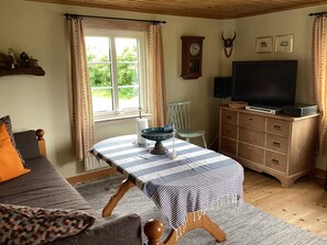 A cozy room with a bed, a table with a striped tablecloth, a television, a clock, and a wooden cabinet. - 6 Person Holiday Home in Vessigebro (Vessigebro)