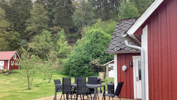 Ein rotes Gebäude mit einer Terrasse, Sitzgelegenheiten im Freien und Blick auf eine bewaldete Landschaft.