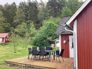 Ein rotes Gebäude mit einer Terrasse, Sitzgelegenheiten im Freien und Blick auf eine bewaldete Landschaft.