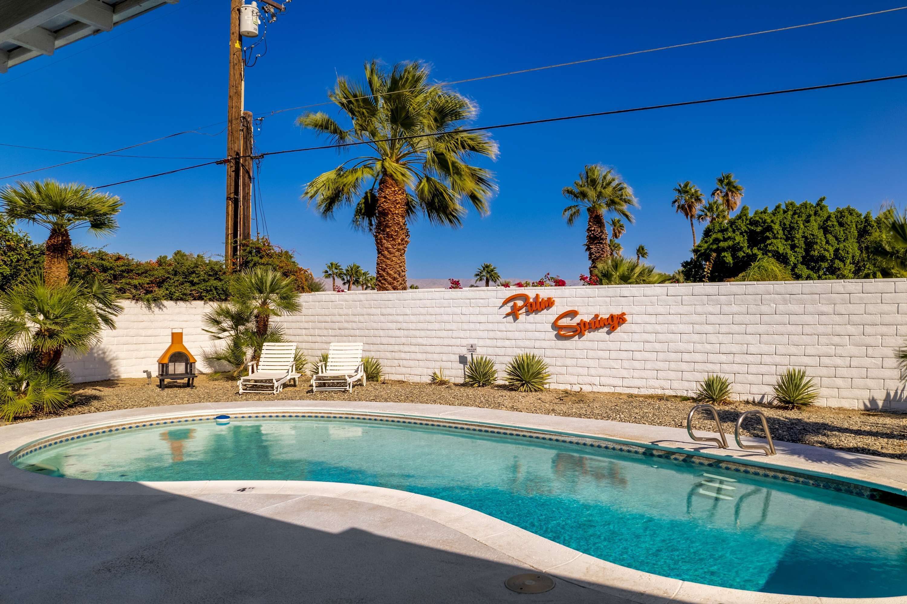 A swimming pool with lounge chairs and palm trees.