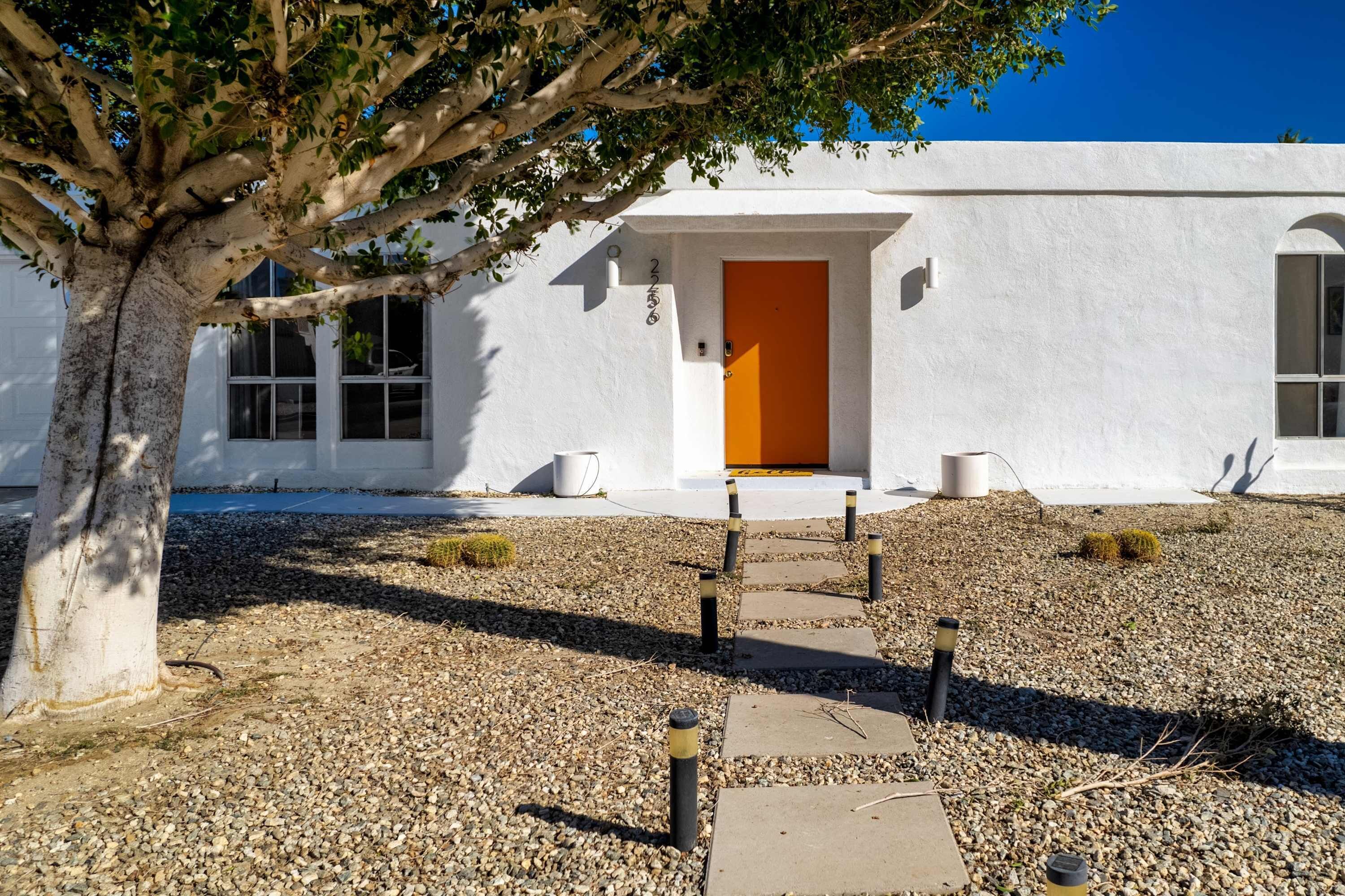A white building with a tree in front, a gravel path, and a door.