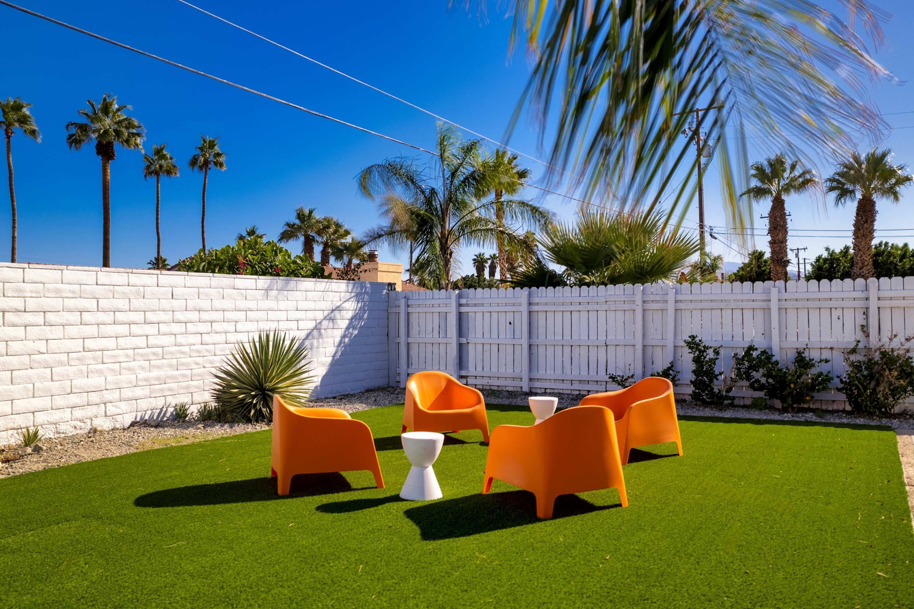 A patio area with artificial grass, orange chairs, and a white fence.
