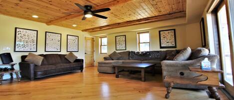 A spacious living room with wooden flooring, a ceiling fan, and a large window providing natural light.