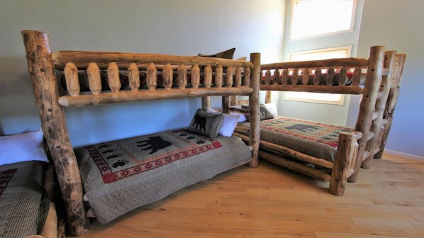 Ein rustikales Etagenbett aus Holz mit einem gemusterten Bettbezug und Kissen, in einem Zimmer mit Holzboden und einem Fenster.