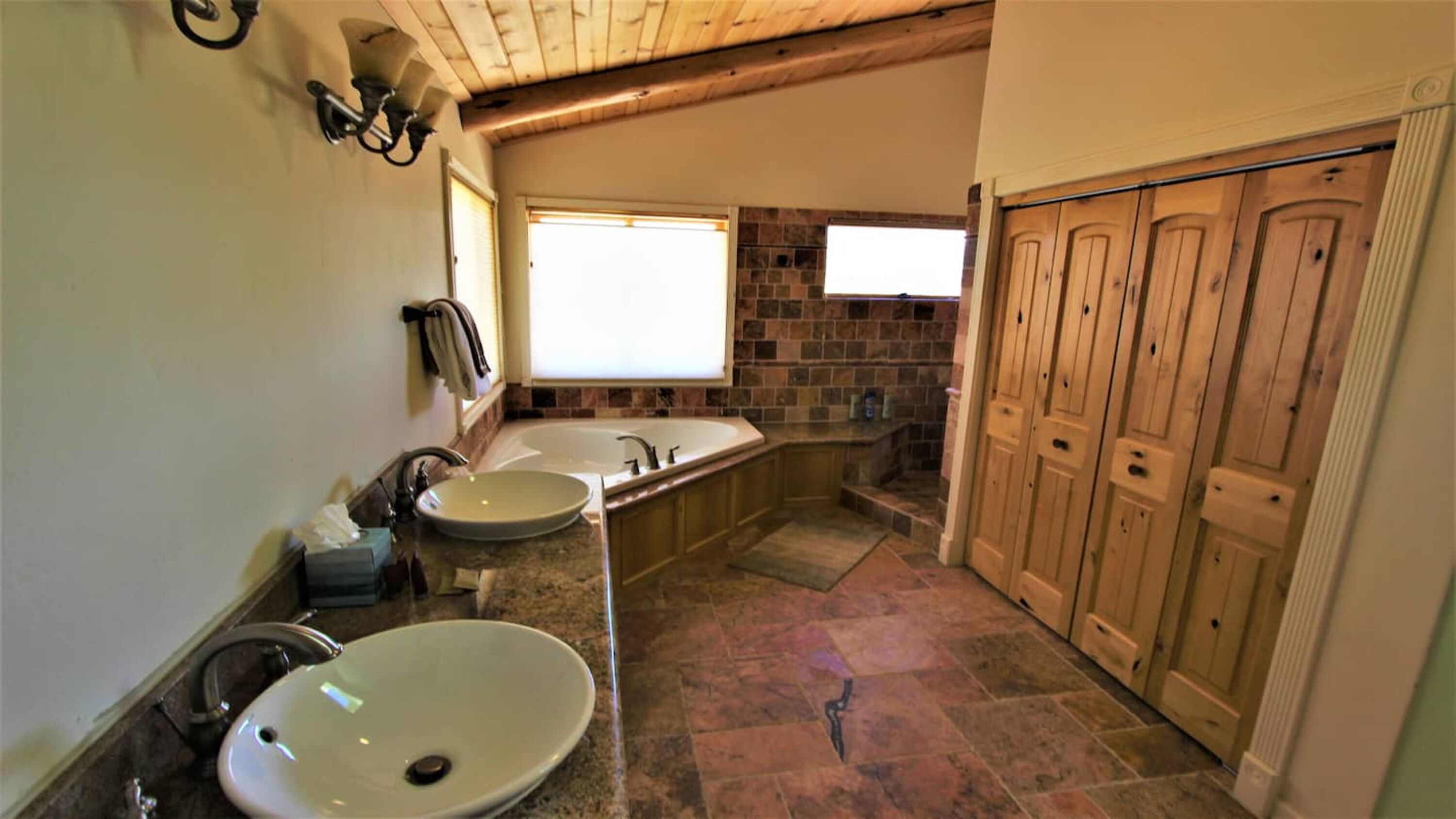 Un baño con dos lavamanos, una bañera y taquillas de madera.
