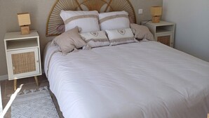 A neatly made bed with a headboard, two bedside tables with lamps, a woven nightstand, and a patterned rug. - New, fully-equipped F2 gite in secure grounds (Hérépian)