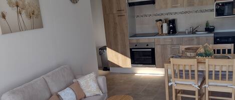 A modern kitchen with wooden cabinets, a dining area with a wooden table and chairs, and a living area with a sofa and a small wooden stool.