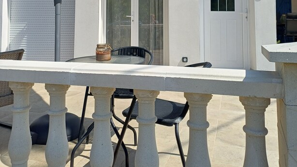 A patio with a table and chairs, a large umbrella, and a white door with decorative elements. - New, fully-equipped F2 gite in secure grounds (Hérépian)