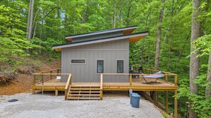 A small cabin with a deck, surrounded by forest.