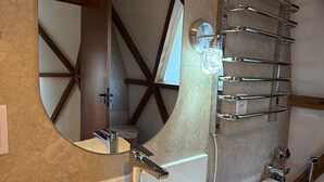 Un baño con un espejo redondo, un lavabo blanco y un perchero para toallas.
