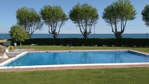 Ein rechteckiger Pool mit klar blauem Wasser, umgeben von einer gepflegten Rasenfläche und mehreren Bäumen.