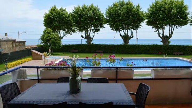 Eine Terrasse mit Tisch und Stühlen mit Blick auf einen Swimmingpool und das Meer.