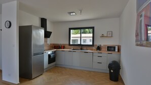 A modern kitchen with a stainless steel refrigerator, microwave, and oven. There is a window providing natural light and a trash bin.