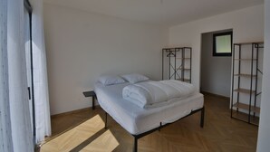 A bedroom with a bed, a wooden floor, a white wall, and a door with a curtain.