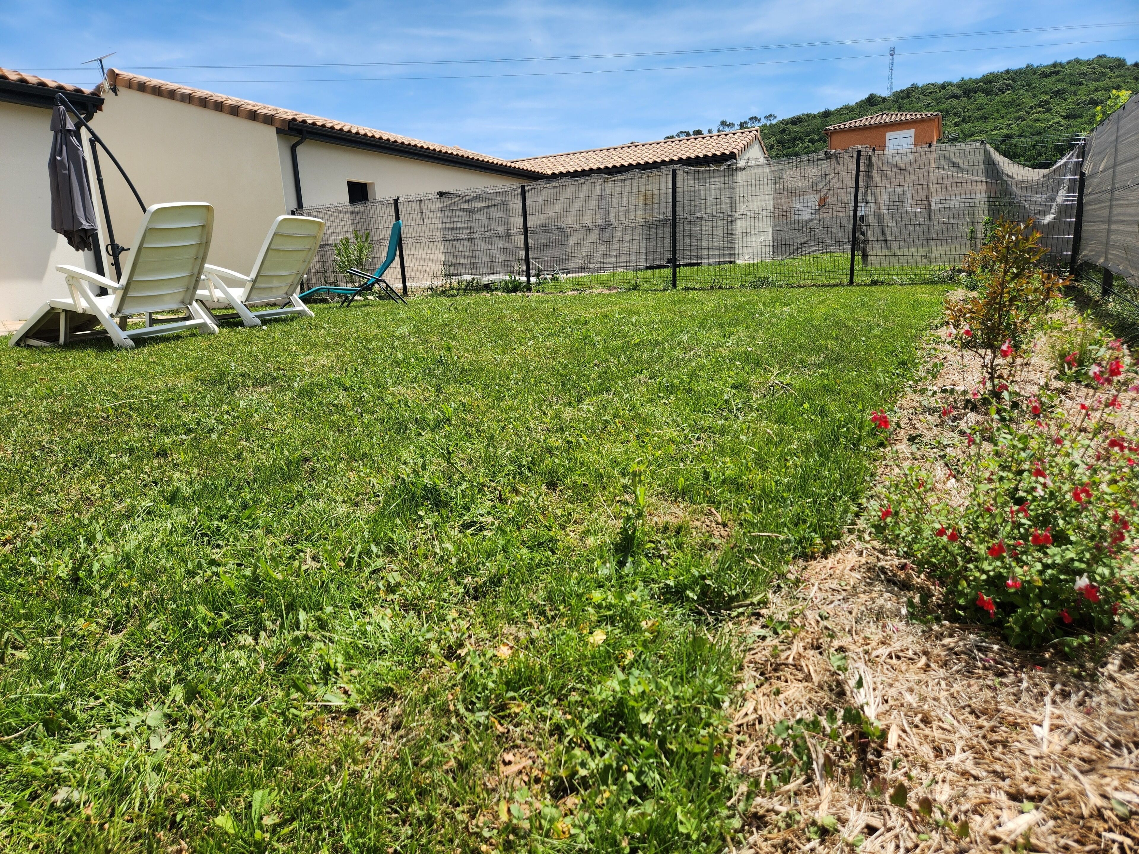 A grassy backyard with a fence, a white building, and two white chairs.