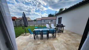 A patio with a glass table and chairs, a barbecue grill, and a view of a residential area.