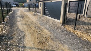 A gravel driveway leading to a gated garage area with a large black garage door.