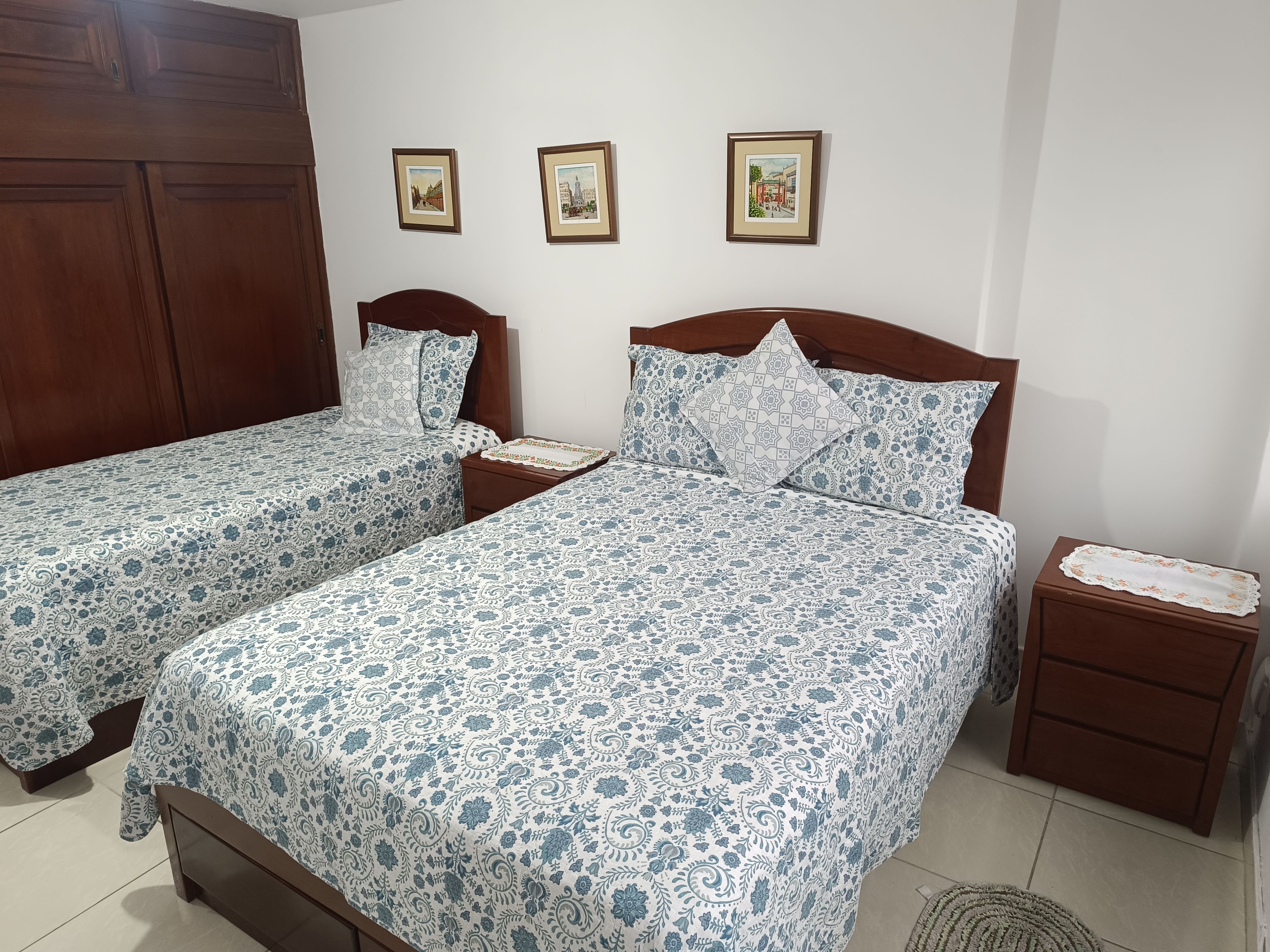 Une chambre avec deux lits simples, des têtes de lit en bois, une table de chevet et une petite table de nuit agrémentée d’un plateau décoratif.