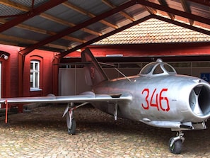 Un avión de combate plateado y antiguo con el número 346 estacionado bajo un edificio rojo con techo de tejas.