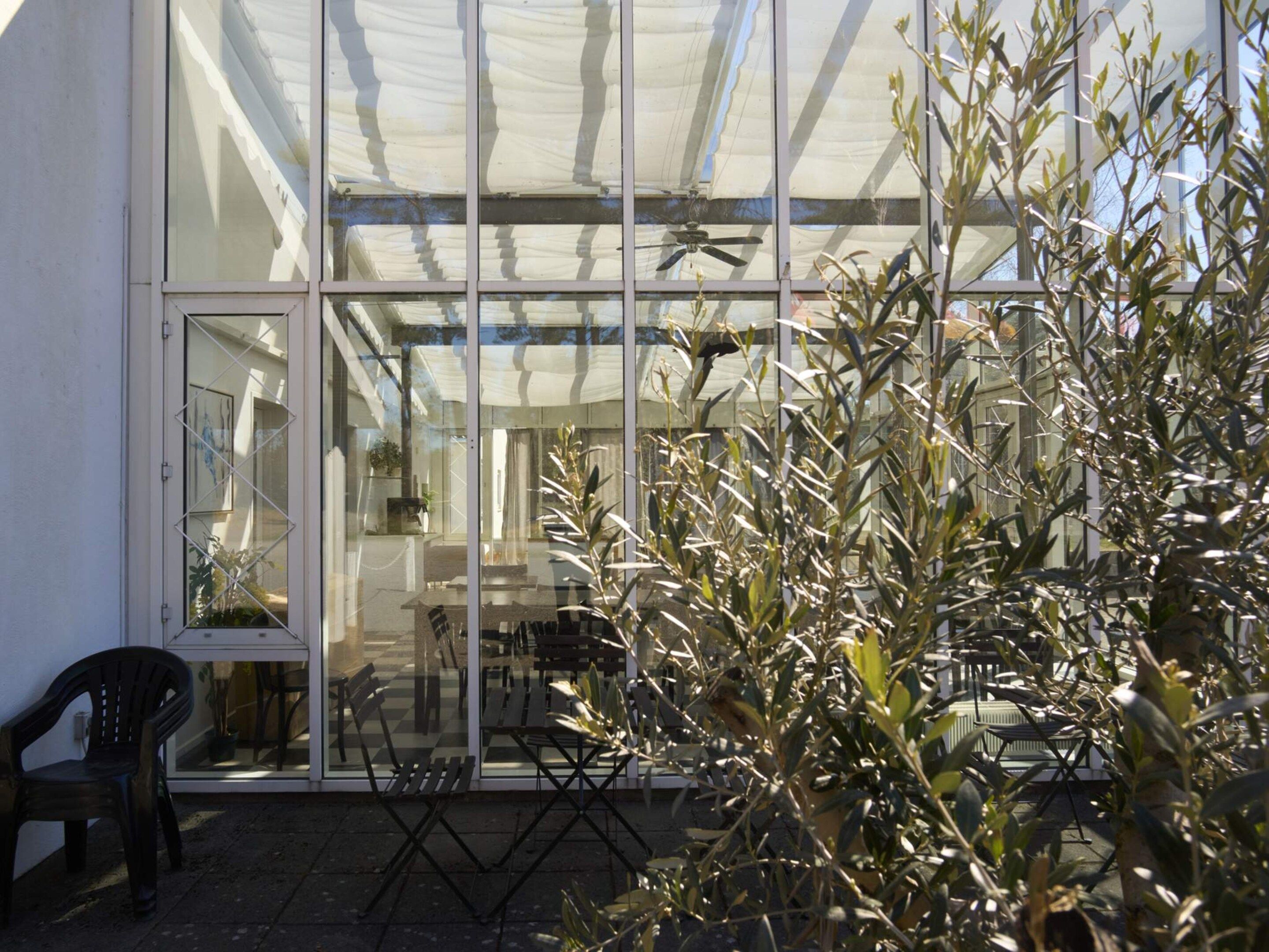 Un invernadero con paredes de vidrio, un ventilador de techo y mobiliario exterior.