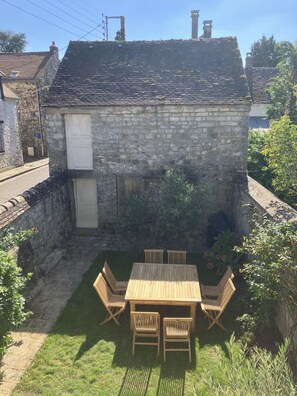 Un bâtiment en pierre avec un petit jardin et une table en bois entourée de chaises.