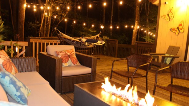 An outdoor patio with wicker furniture, a fire pit, and string lights.