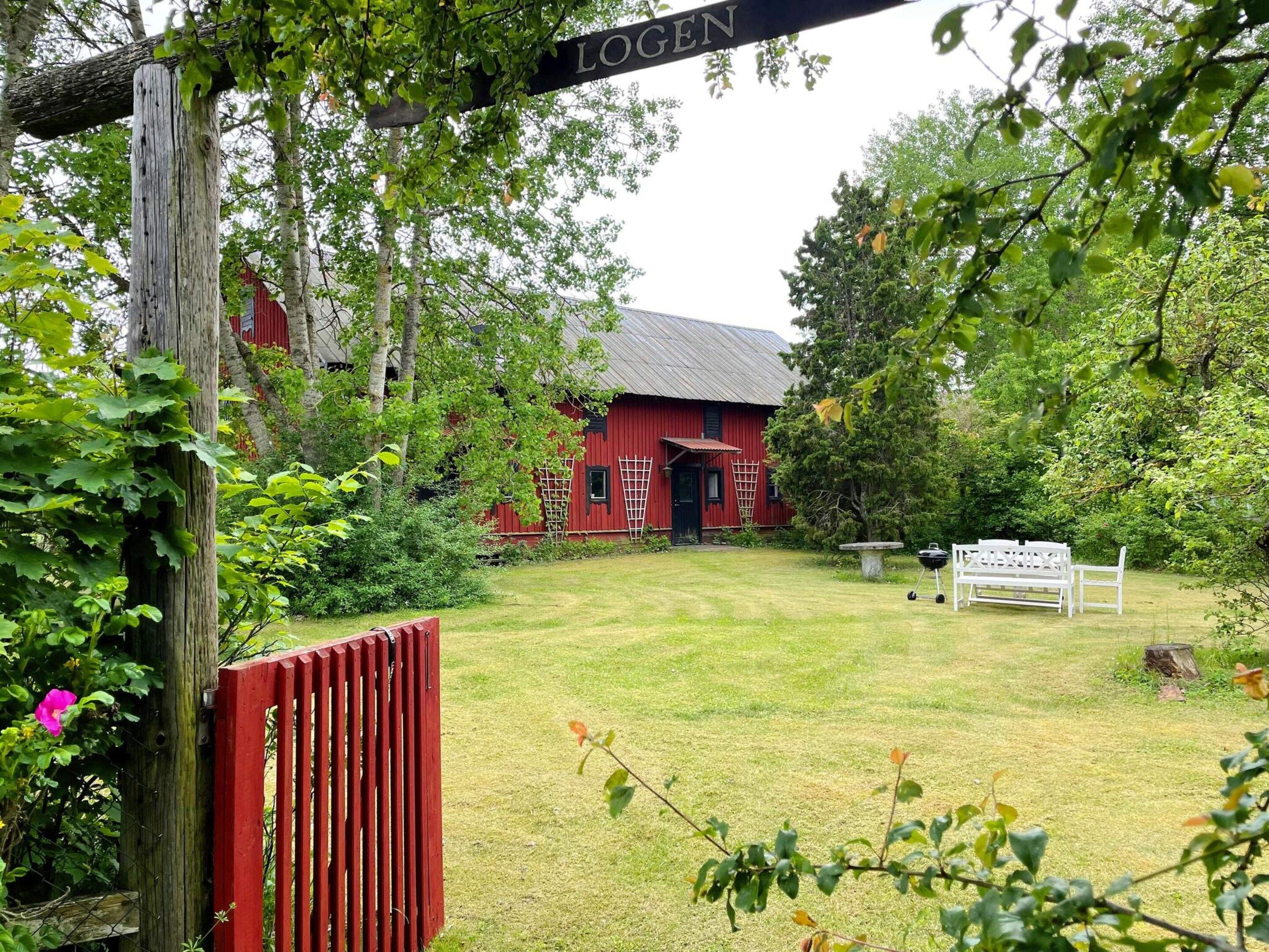 A red barn with a black roof, surrounded by a grassy yard and trees.