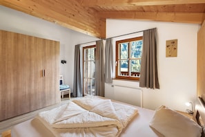 A bedroom with a bed, wooden wardrobe, window with curtains, and a chair.
