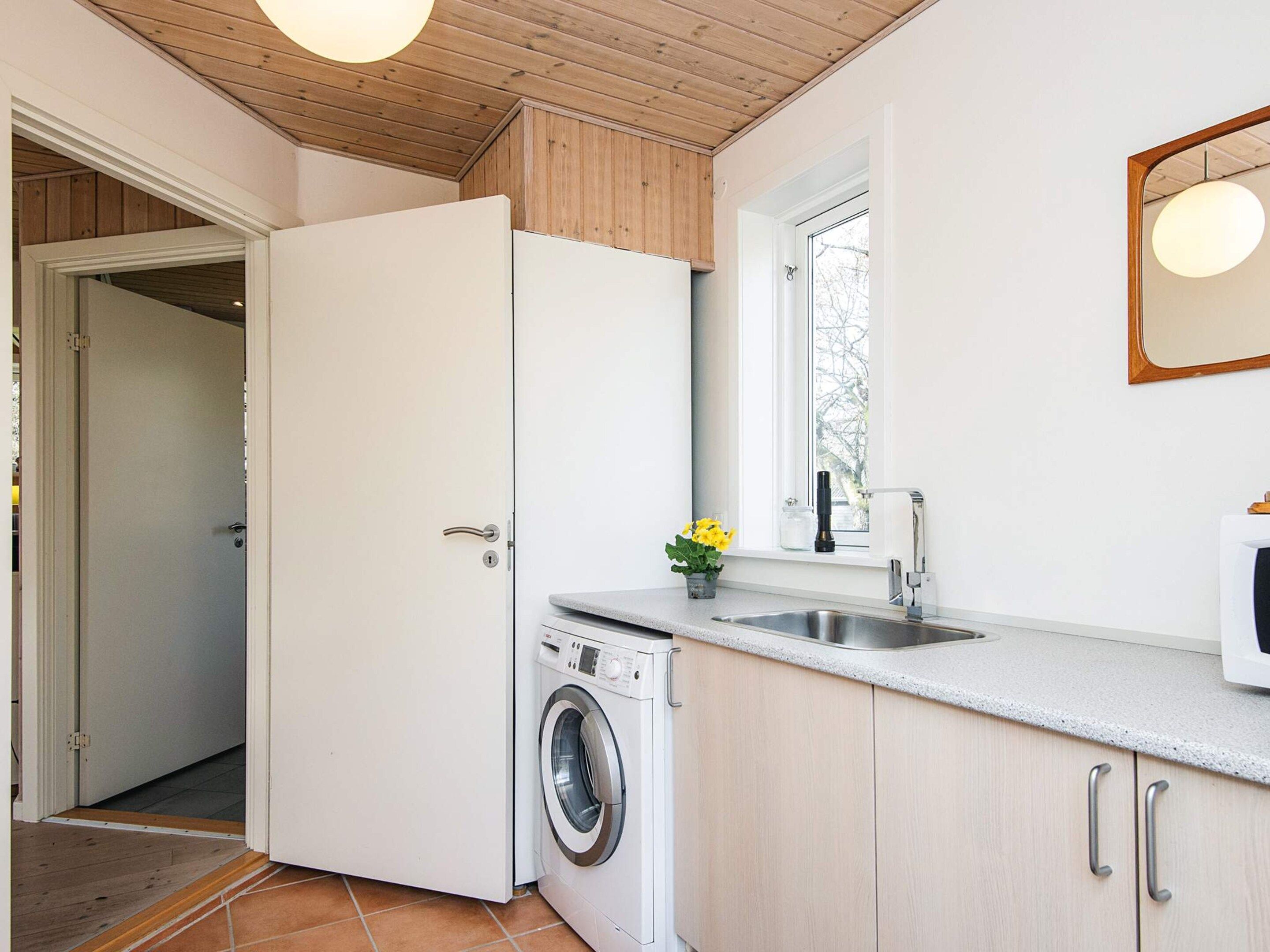 A compact kitchen with a washing machine, a sink, and a window.