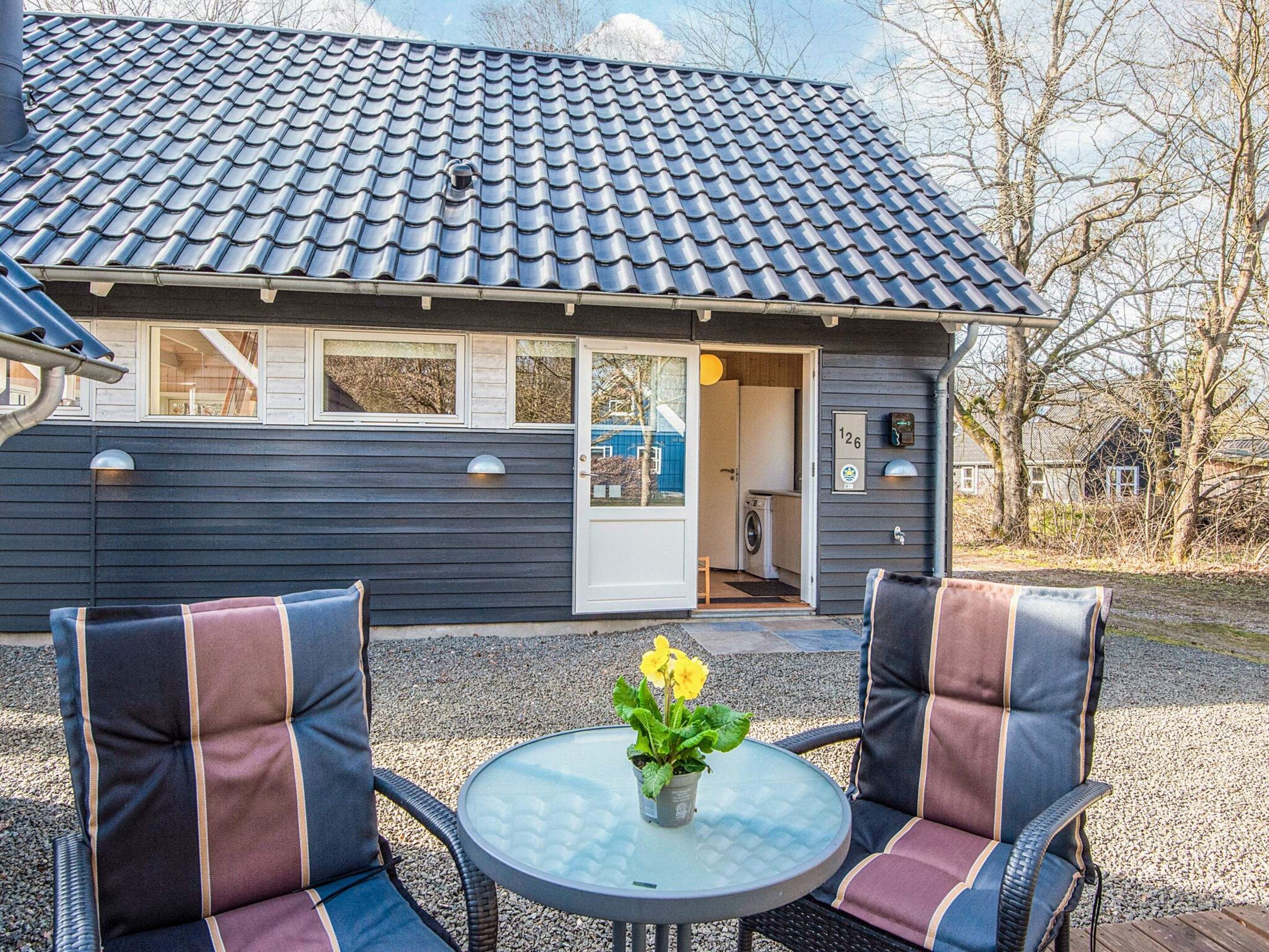 A house with a tiled roof, a door, and a window. There is a table with chairs and a potted plant.