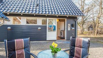 A house with a tiled roof, a door, and a window. There is a table with chairs and a potted plant.