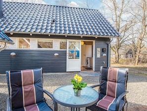 A house with a tiled roof, a door, and a window. There is a table with chairs and a potted plant.