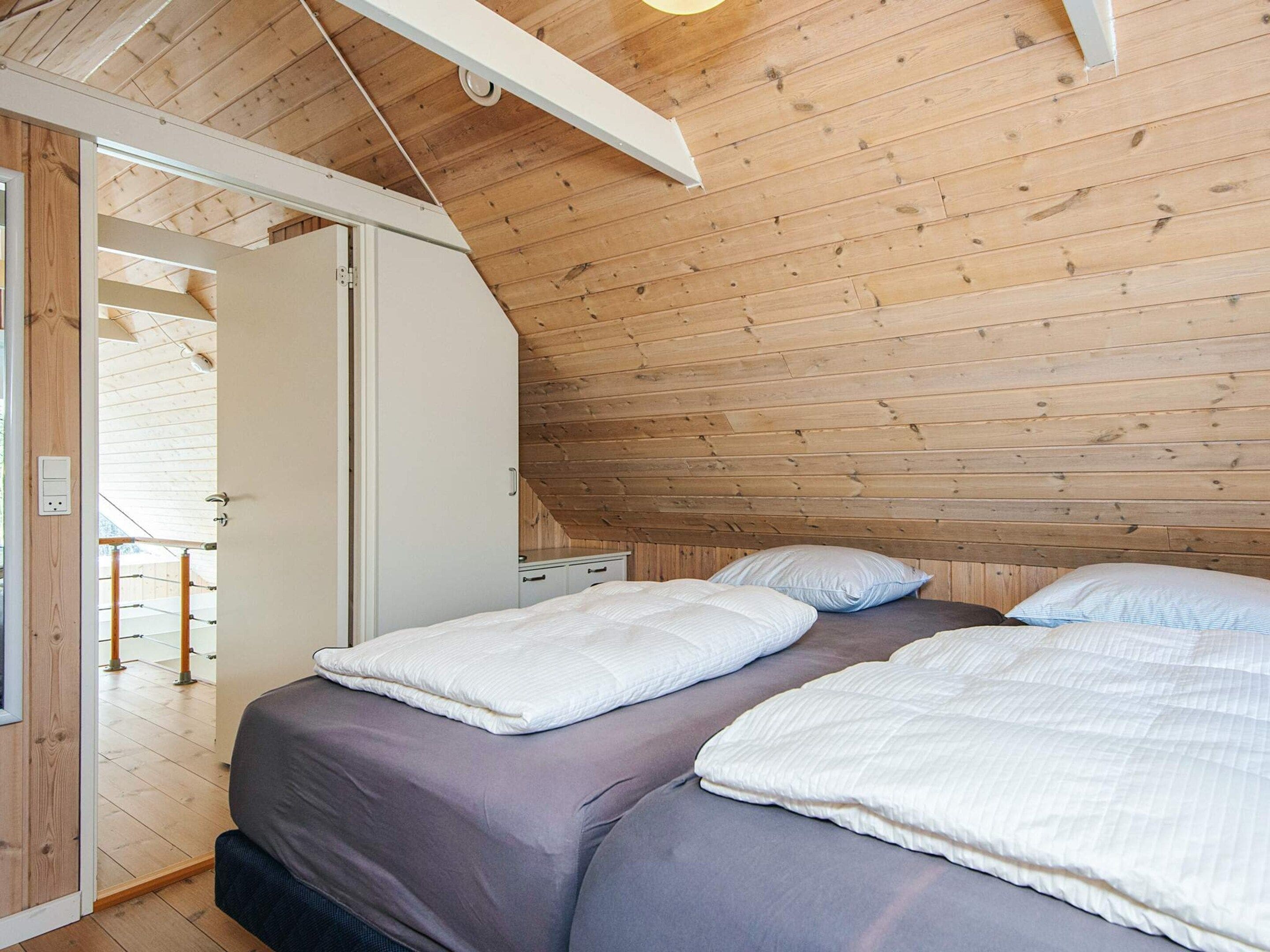 A bedroom with a sloped ceiling, wooden walls, a bed with white and grey bedding, and a door leading to a balcony.