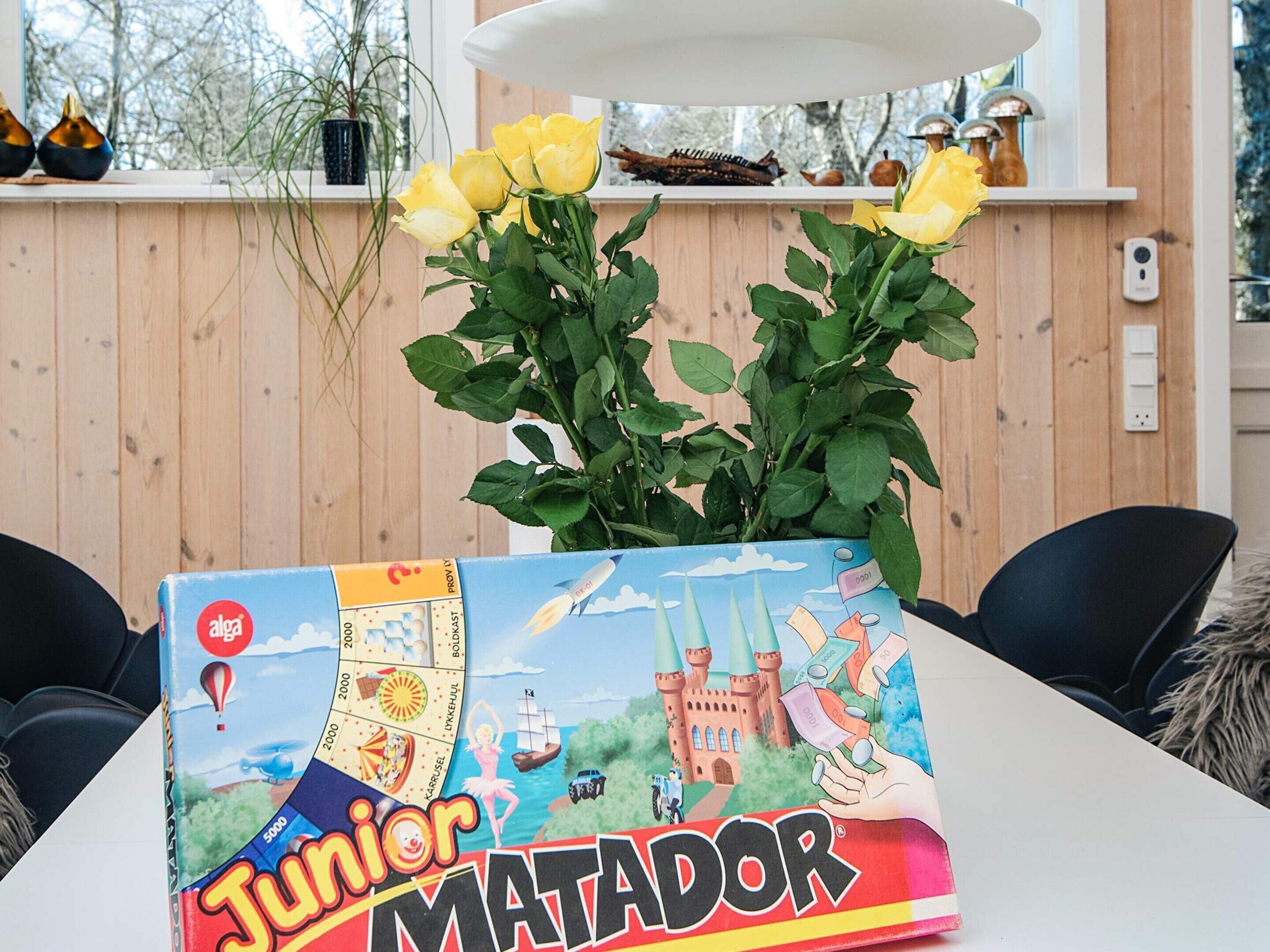 A table with a board game box titled "Junior Matador" and a potted plant with yellow flowers.