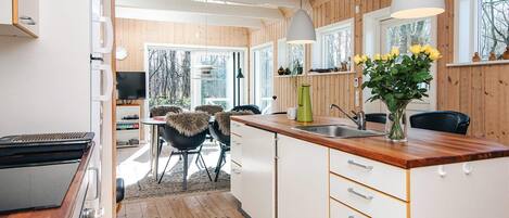A modern kitchen with wooden flooring, white cabinetry, and a dining area with chairs and a table.